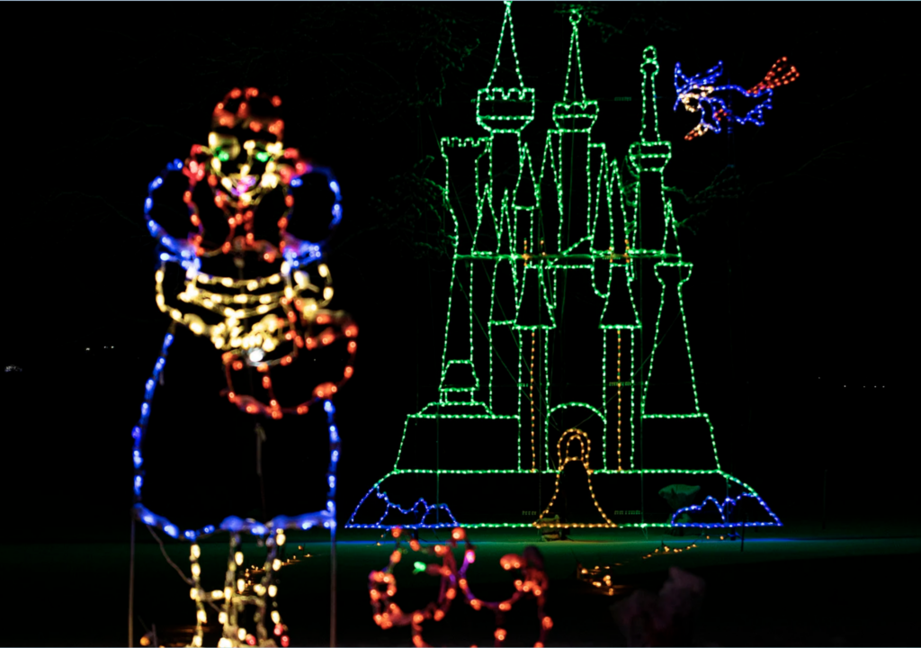 A figure that resembles a person is made out of christmas lights in the background is a castle also made out of green christmas lights. 